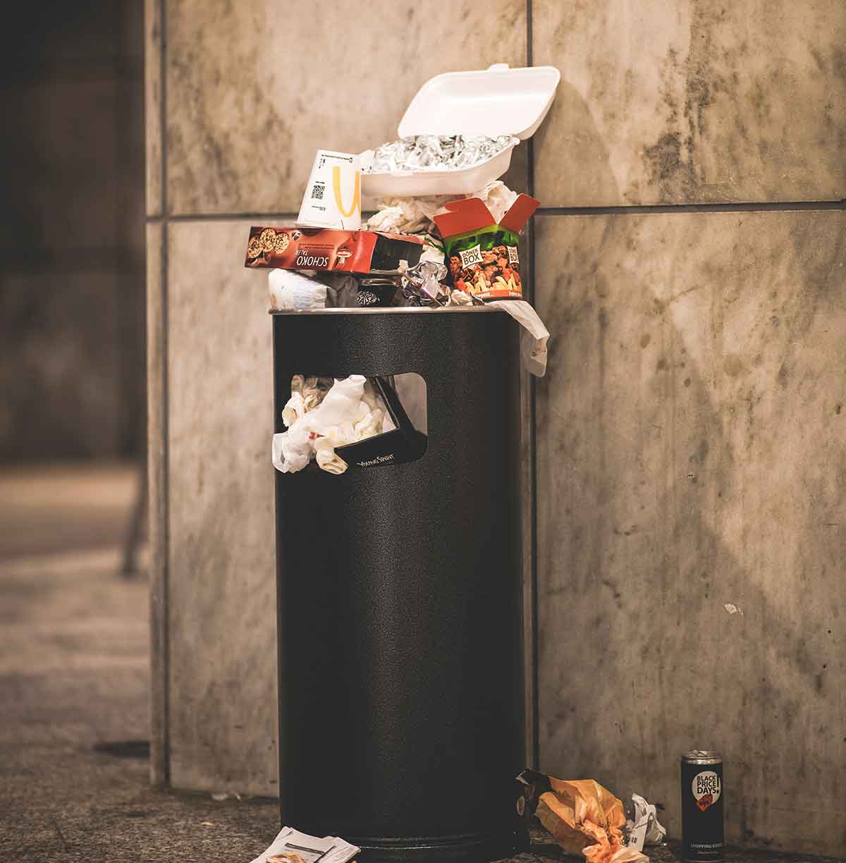 Trash can on a concrete wall that is overflowing with garbage.