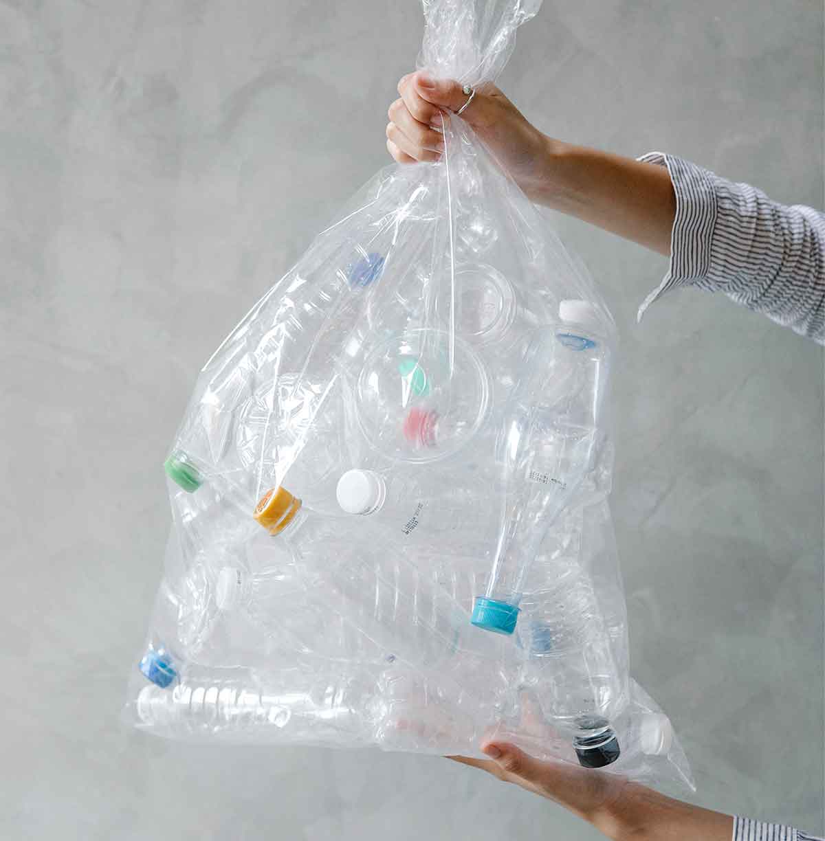 Women's hands holding a clear garbage bag with recyclable bottles.