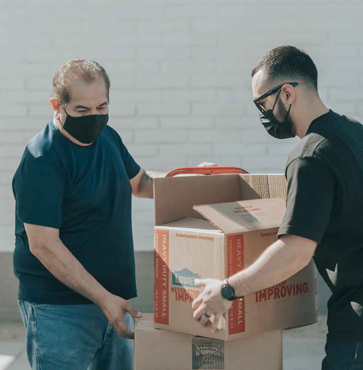 two men with medical masks moving open boxes