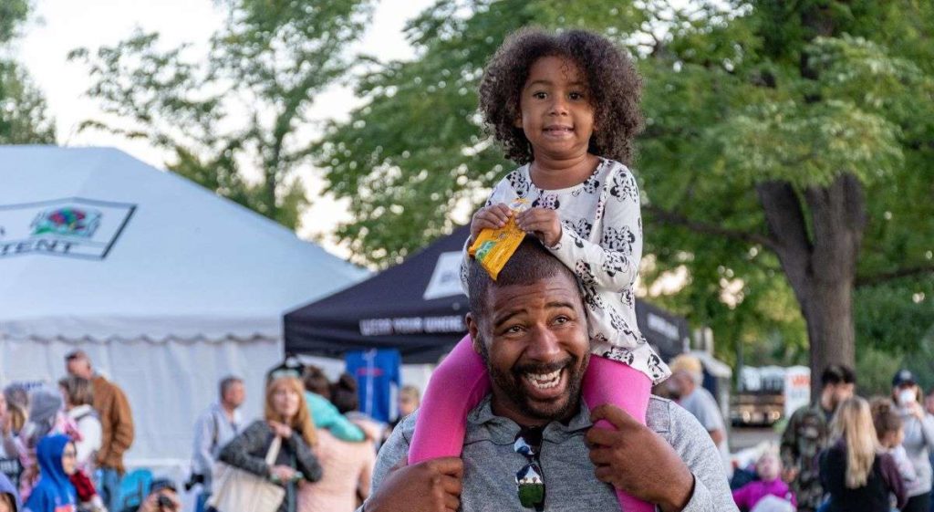 Father with his daughter on his shoulders at an outdoor festival.